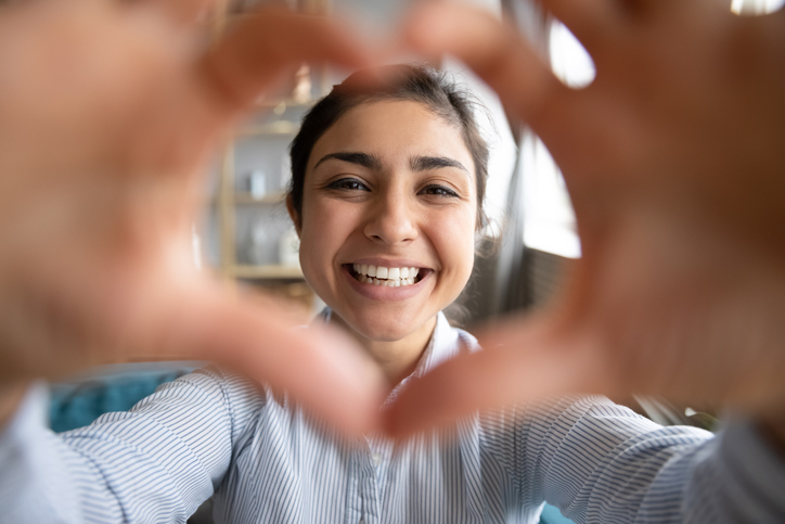 Cute happy indian girl making heart shape hand gesture looking at camera, funny smiling ethnic young single woman blogger laughing face showing love sign symbol, dating concept, close up portrait