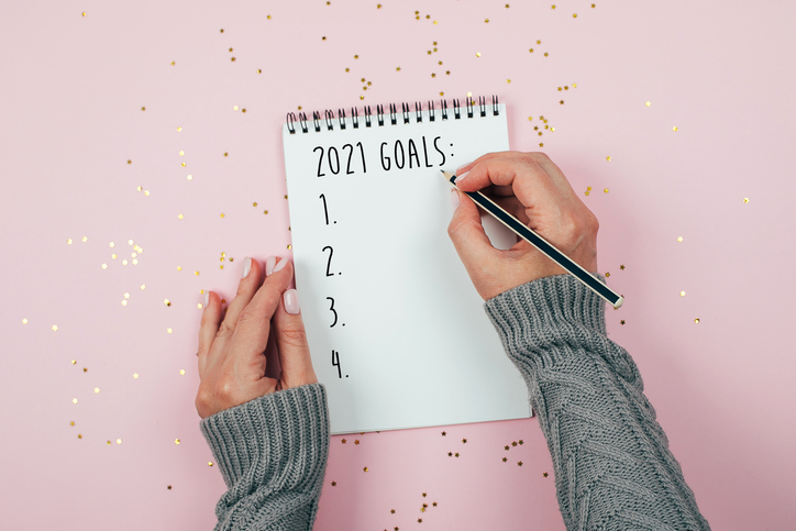 Happy New Year 2021. Woman's hand writing 2020 Goals in notebook decorated with Christmas decorations on the tricolor background. Top view, flat lay