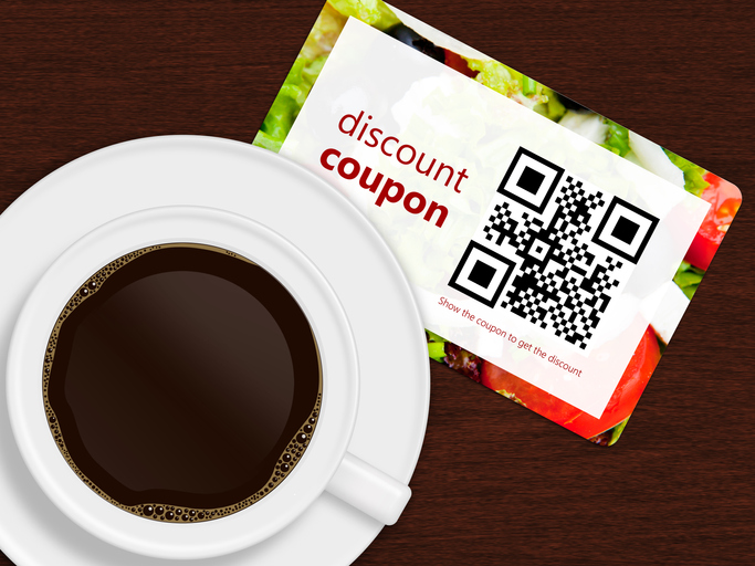 cup of coffee with discount coupon lying on wooden desk. photo of food is author's property. qr code is designed and generated by author.